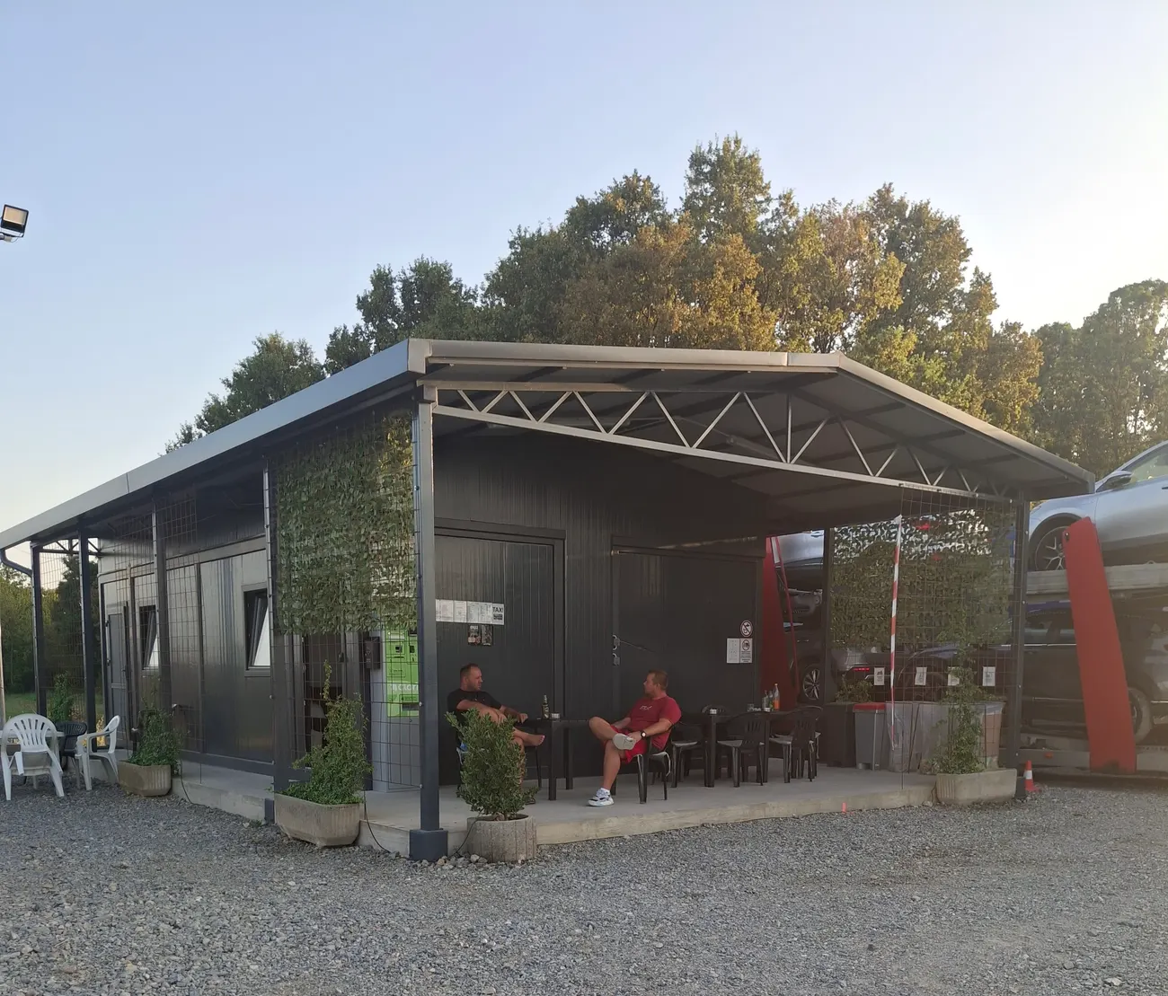 Tamna montažna zgrada s natkrivenom terasom, dva vozača sjede za stolom